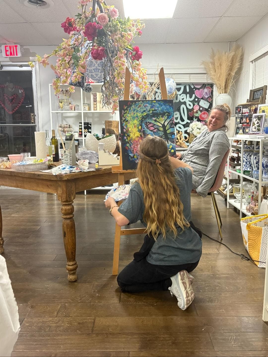 Ally Nowakowski kneeling beside a workshop participant to help adjust a painting.