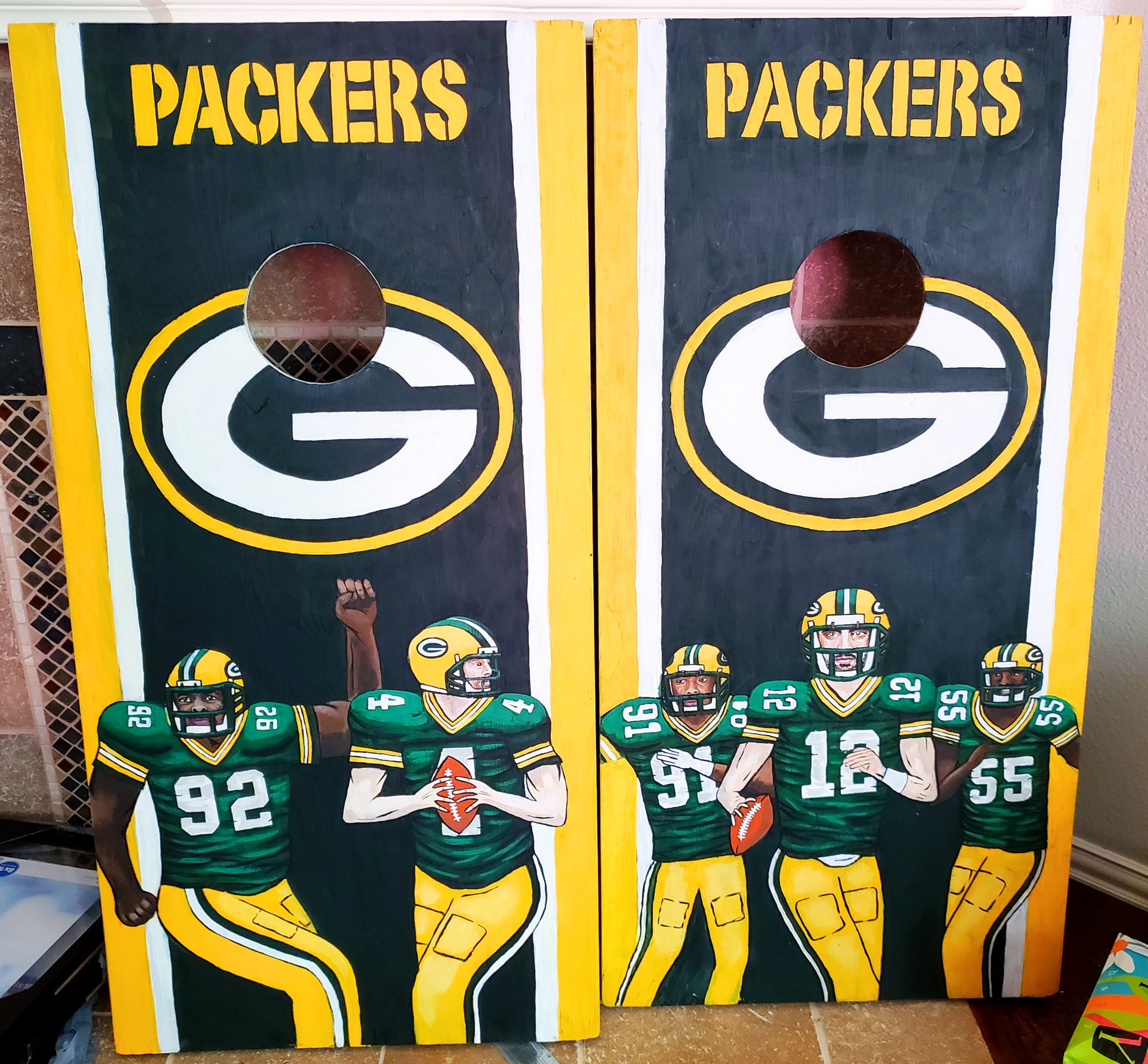 Two custom Green Bay Packers corn hole boards painted with team logos and player illustrations, by Ally Nowakowski.