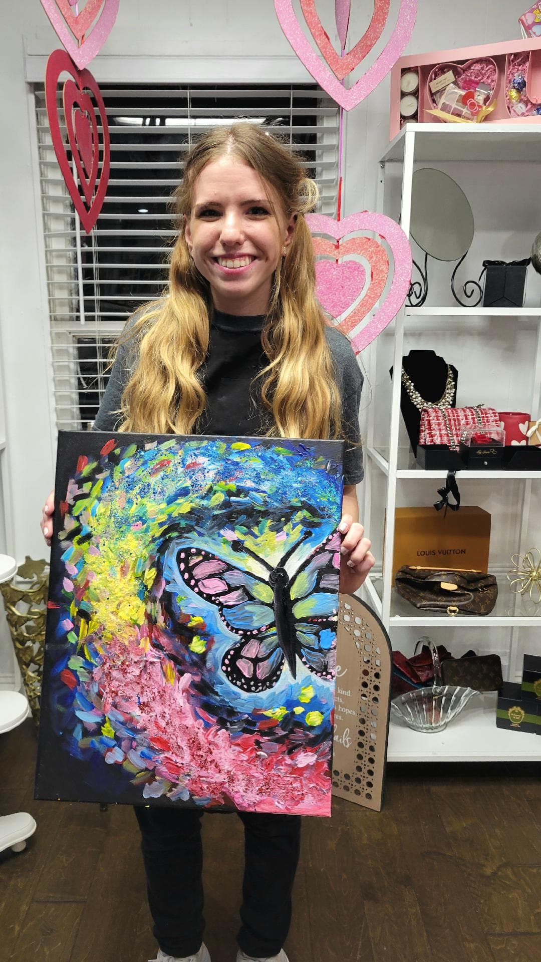 A workshop participant holding up her finished butterfly painting with a smile.