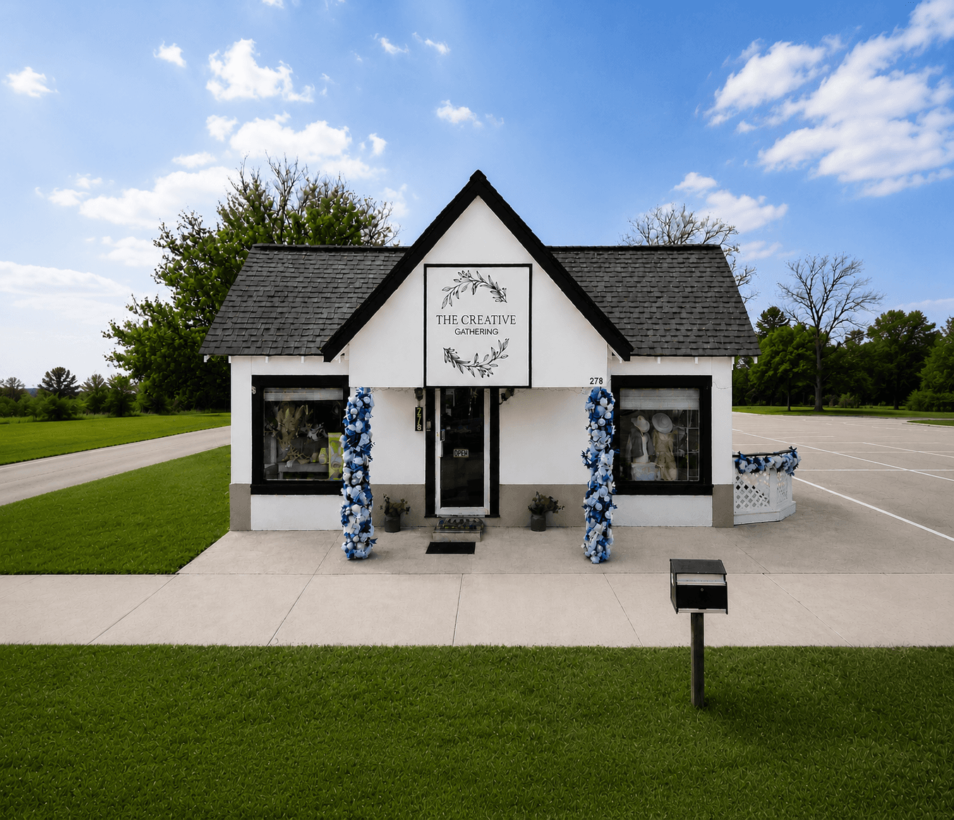 The Creative Gathering, workshop venue in Lake Dallas, Texas. A white cottage with black trim and blue floral arrangements framing the front door.